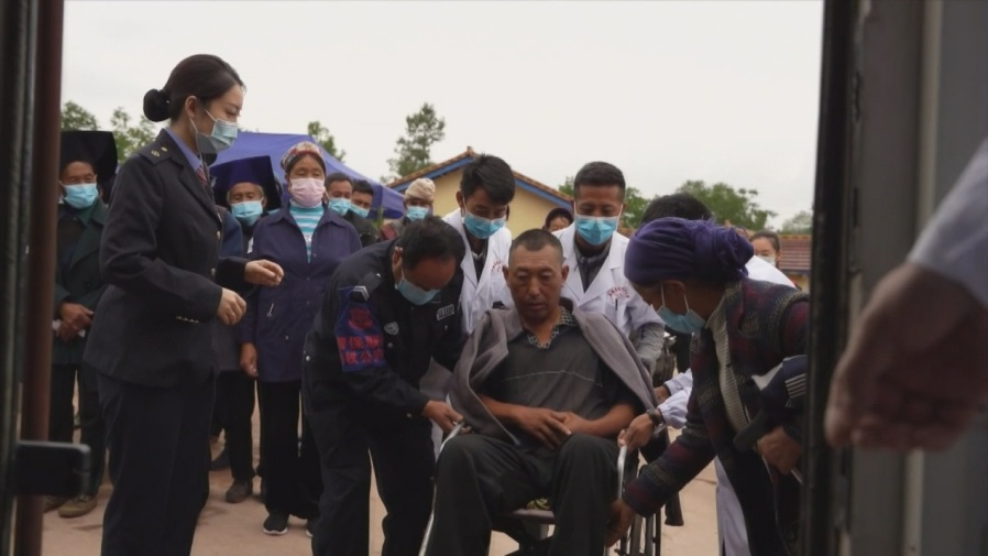 患有半身不遂的村民吉约沙果坐着轮椅前来检查身体，工作人员把他抬到健康列车上进行诊疗。